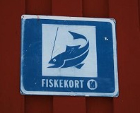 Vit och blå skylt på röd husvägg, blå fisk samt vit text FISKEKORT